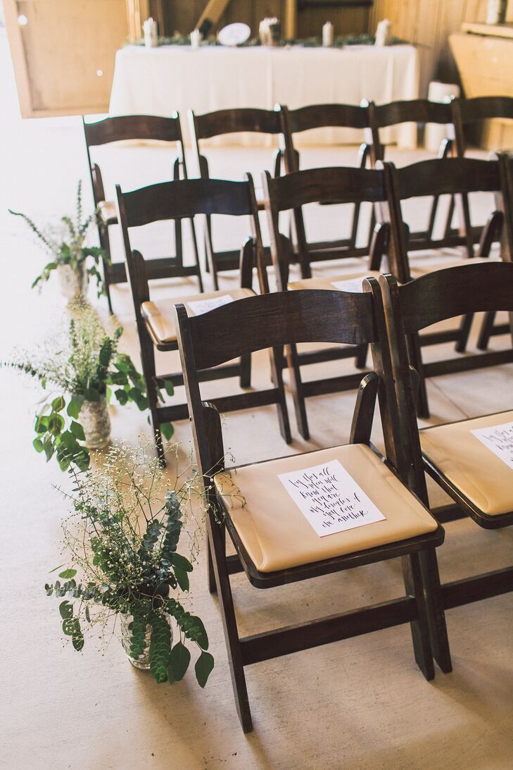 The ceremony took place inside the barn at Camarillo Ranch in Camarillo, California, where wooden folding chairs were lined up to face the altar. A black-and-white program with calligraphy was placed on each chair, and the aisle was lined with floor arrangements of greenery and eucalyptus.