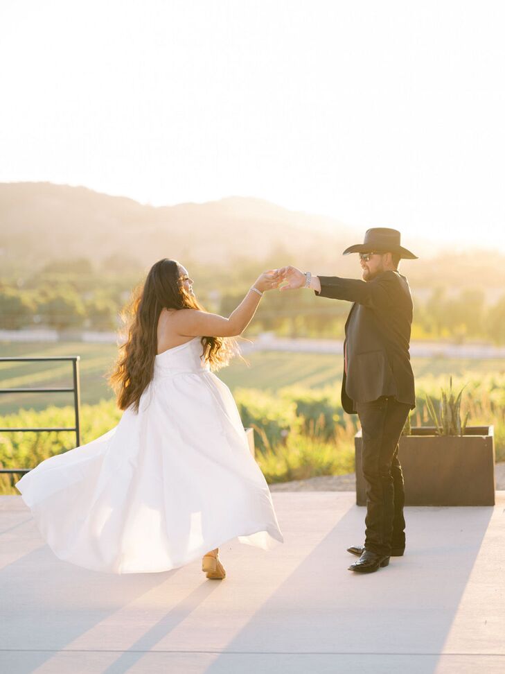 Groom in Black Suit and Cowboy Hat Twirls His Bride in Flowing Dress at Summer Ranch Wedding