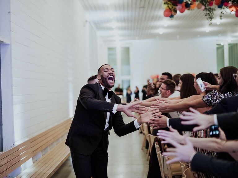 Grooms running down a high-five line at wedding. 