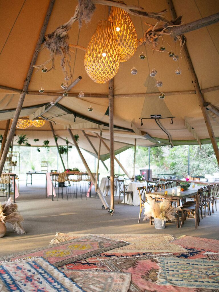 Layered boho rugs inside wedding tent with macramé lighting and clusters of branches