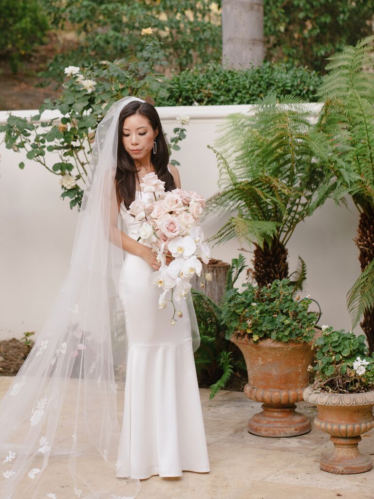 bride stands in courtyard holding modern cascading wedding bouquet with blush roses and white phalaenopsis orchids