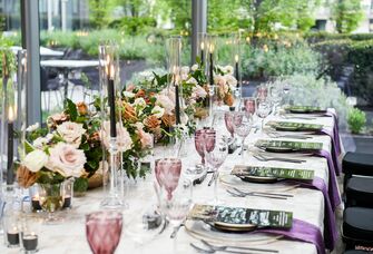 modern romantic wedding tablescape with low rose centerpieces, black taper candles, menu cards, purple water goblets and linen napkins