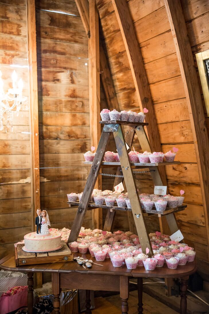 The one-tier cake and cupcakes were displayed on a vintage wooden table. To make more space, Hannah and Caleb set up a rustic wooden ladder on top of the table to make little shelves for the desserts. They wanted this area of the barn to be a little more romantic, so they hung a crystal chandelier next to the display.