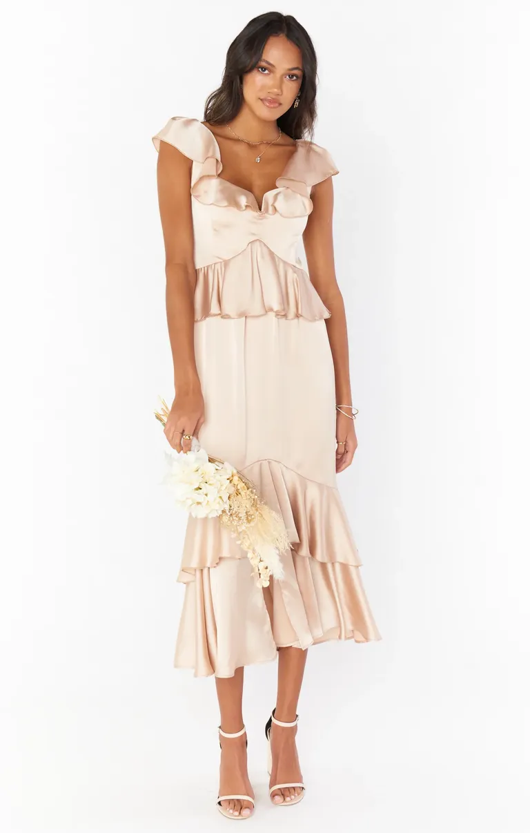 Model wears a lace mid-length gow with a ruffled hem and waistline. 