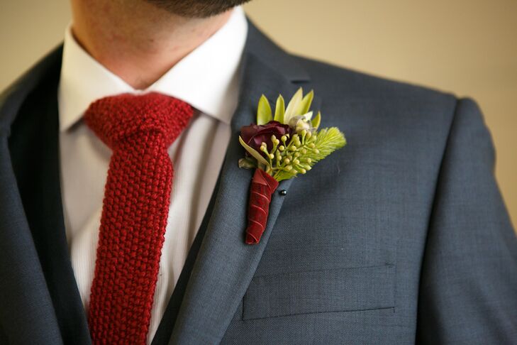 Jackson wore a gray suit with a red knit tie. His boutonniere had a single red rose with greenery,  with a red velvet boutonniere wrap to complete his winter style.