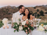 Couple sitting at reception table laughing with mountain background