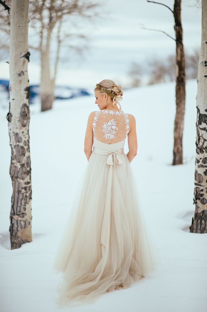 Suzi wore designer Catherine Deane’s Onyx gown for her winter nuptials. She loved the flowing tulle skirt and the white lace detailing on the back. She completed her look with a champagne satin belt and a wintery green and gold flower crown.