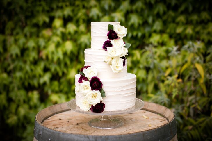 The wedding cake -- a three-tiered structure sitting on a vintage glass pedestal -- was simply decorated with a smooth, buttercream ring design and a cascade of white garden roses and chocolate cosmos flowers and placed on an antique wine barrel.