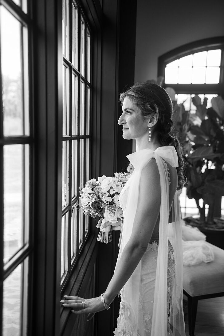 Black and White Photo of Bride With Tulle Bows on Shoulders, Bouquet, Looking Out Window