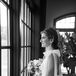 Black and White Photo of Bride With Tulle Bows on Shoulders, Bouquet, Looking Out Window