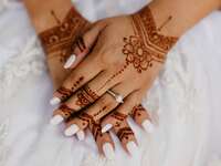 Snapshot of a beautiful white manicure on hands adorned with intricate henna. 