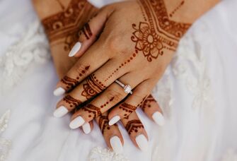 Snapshot of a beautiful white manicure on hands adorned with intricate henna. 