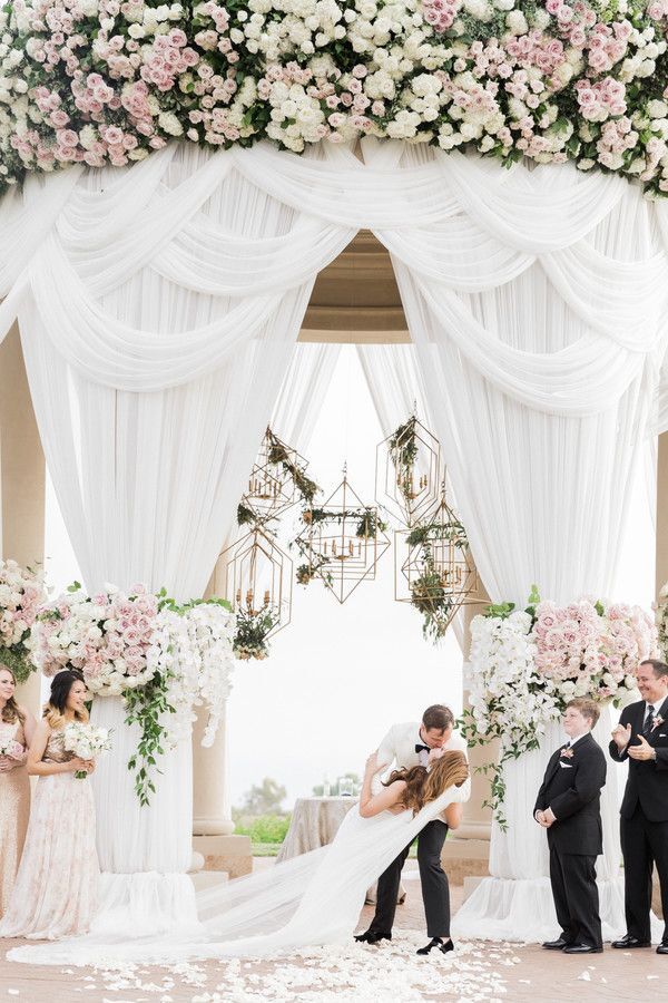 First kiss during wedding ceremony with draping and chandeliers as backdrop