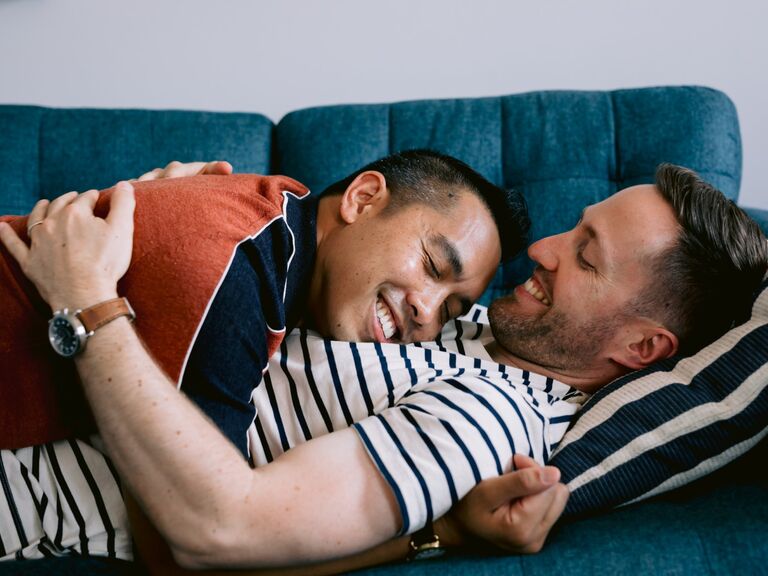 Couple cuddles on their couch while smiling at each other. 