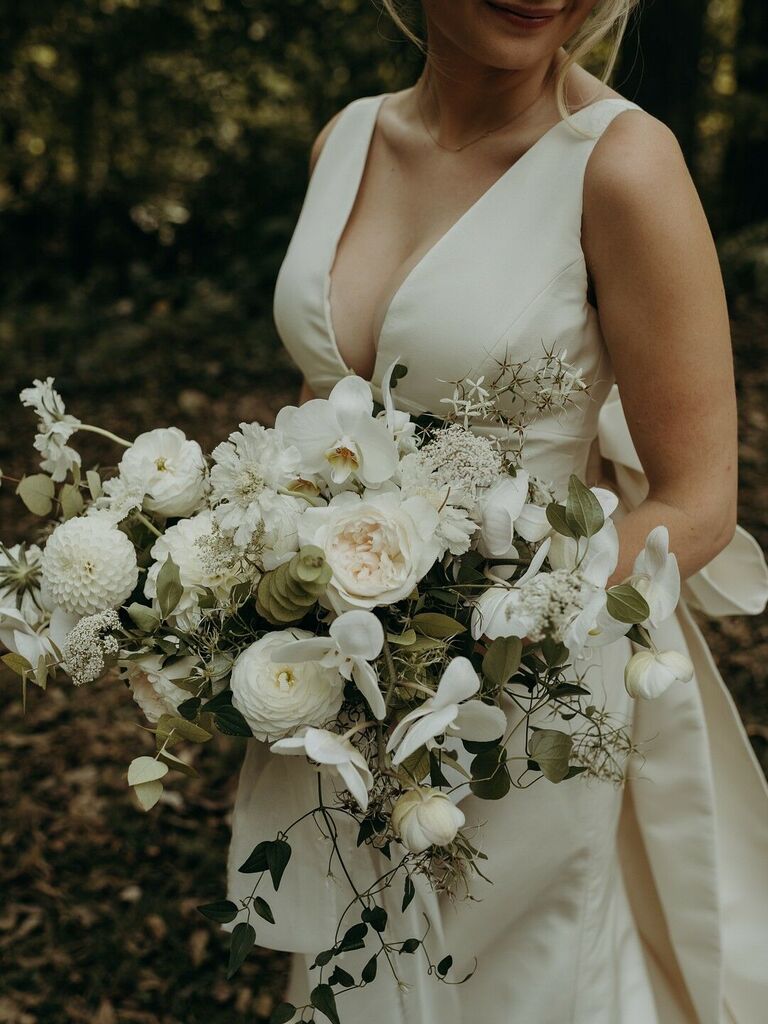 Bride holds a bouquet featuring white dahlias, roses, and greenery. 