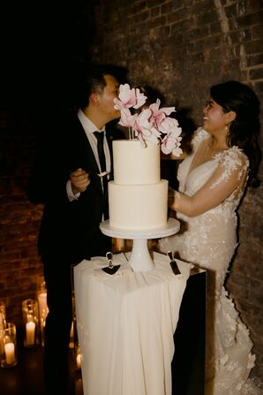 Bride in Fitted Gown and Groom in Black Suit Feeding Each Other Cut Wedding Cake