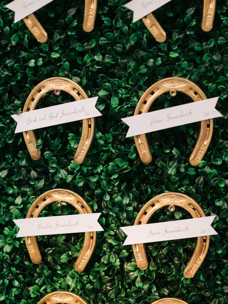 Gold horseshoe escort cards against a lush green backdrop. 