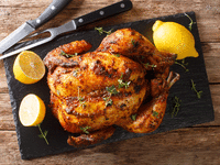 Roasted engagement chicken with lemons surrounding it.