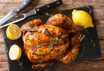 Roasted engagement chicken with lemons surrounding it.