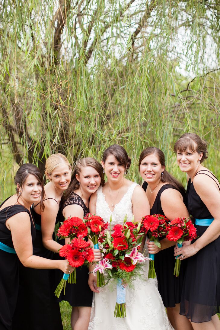 The bride posed with her bridal party, who wore black dresses of their choice and held red bouquets of red gerbera daisies and alstroemeria.