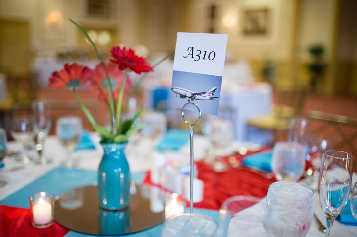 A white card with an airplane model number was used to mark reception tables for guests to match their escort cards with. The card was positioned next to a red daisy assortment in a teal vase.