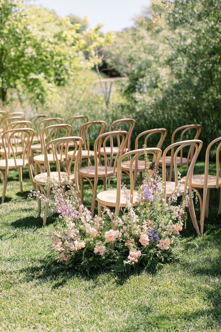 Light Wood Ceremony Chairs on Lawn With Pastel Flower Arrangements