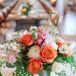 Low, lush arrangements of coral garden roses, football mums, dahlias, astilbe, scabiosa, maidenhair fern, jasmine vine, and silver dollar eucalyptus in gold pedestal vases topped the round reception tables.