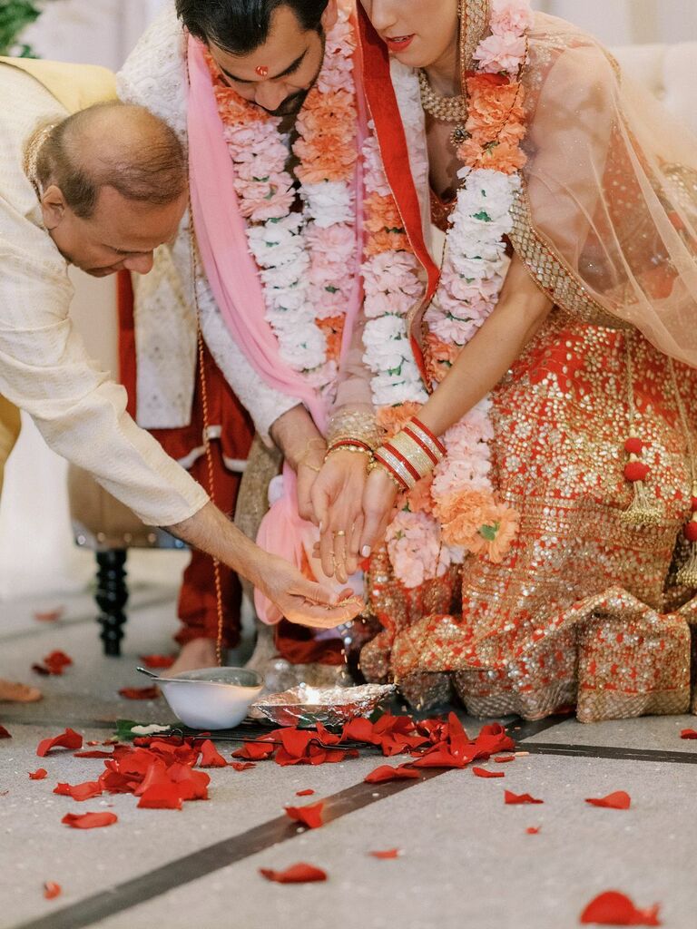 bride and groom performing fire ritual at hindu wedding while wearing floral garlands