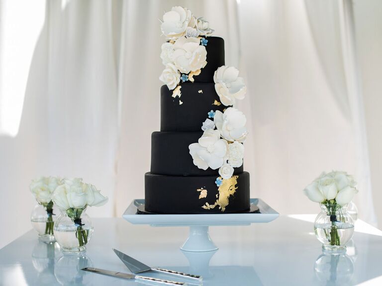 Four-tier black wedding cake with gold foil and white flowers
