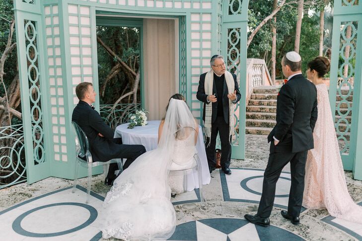 Bride, Groom, Parents and Rabbi Gather Around in Formalwear to Sign the Ketubah at Jewish Ceremony