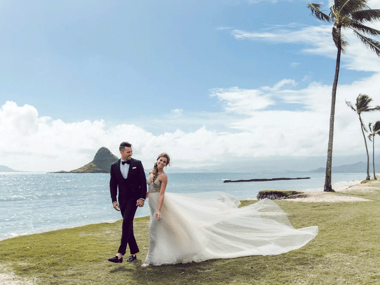 Bride and groom smiling during photoshoot with scenic ocean background.