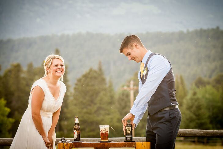 A bride and groom pouring a black and tan drink into a beer glass at their outdoor unity ceremony.