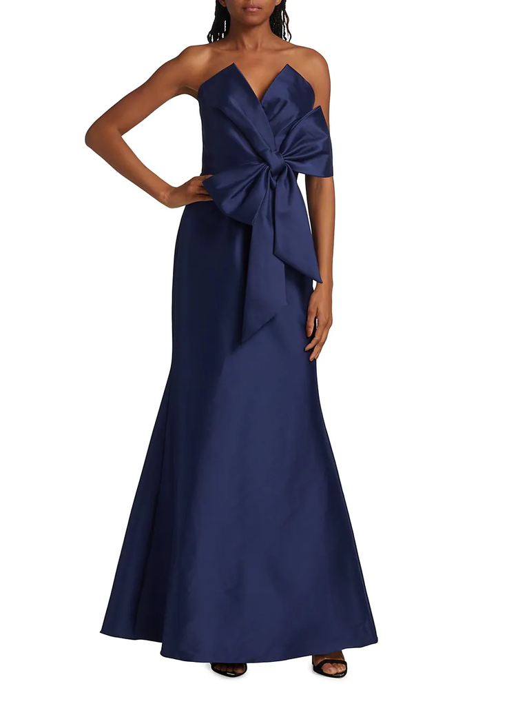 A model wears this sleeveless navy dress with a glamorous V-neck and large statement bow.