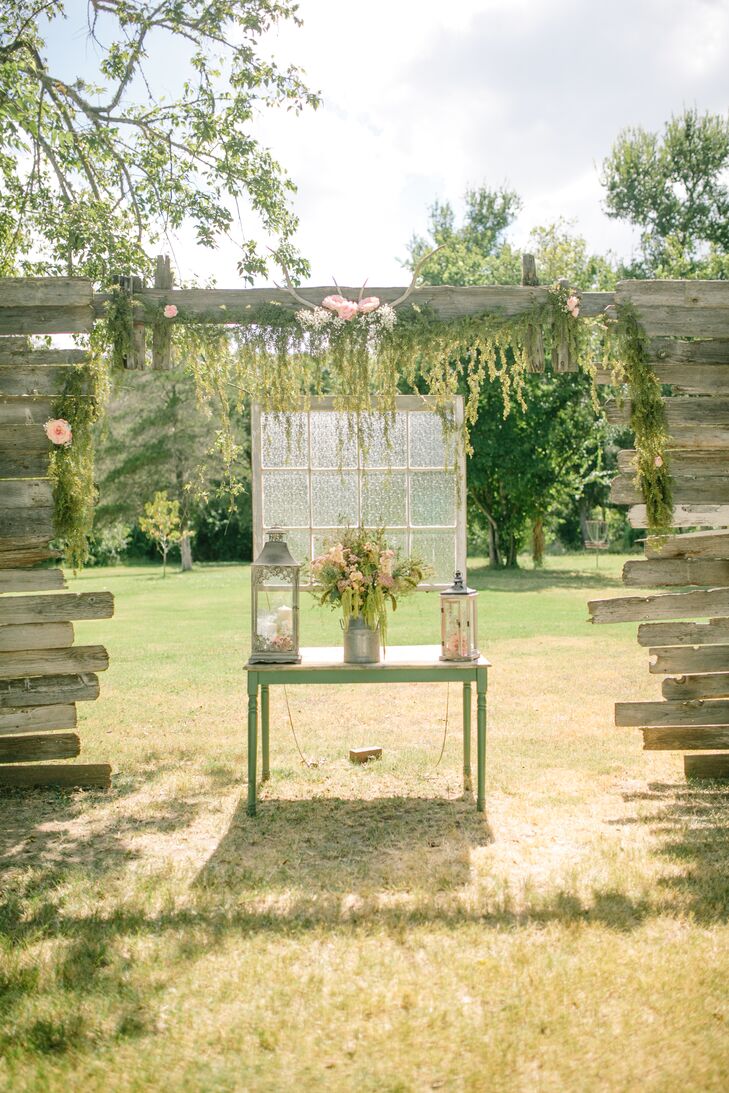 Tylar and Erick decorated the wooden wedding arch with antlers and blush flowers with hanging greenery to enhance the romantic vibe. Underneath, a vintage table with lanterns and an old windowpane created an air of vintage elegance.