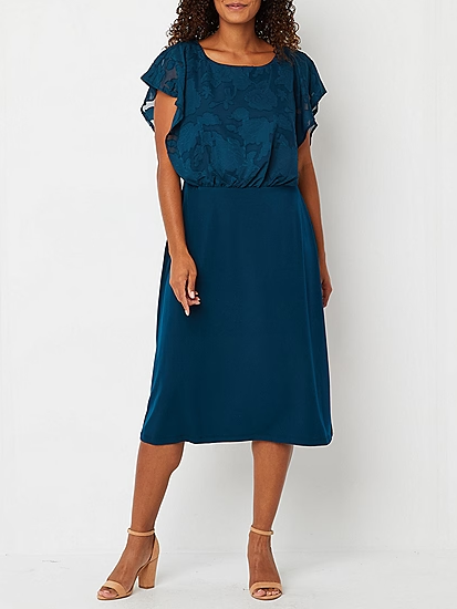 A model shows off a knee-length wedding guest dress with a sleeveless lace bodice.