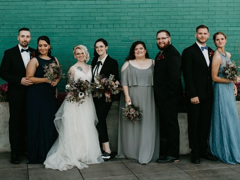 brides posing with bridesmen and bridesmaids in front of painted brick wall