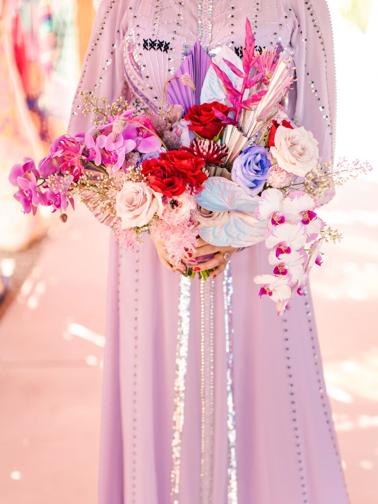 example of 2023 wedding color trend bride wearing light purple dress holding wedding bouquet with hot pink orchids and iridescent ribbons