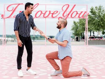 Couple getting engaged in front of pink I Love You sign