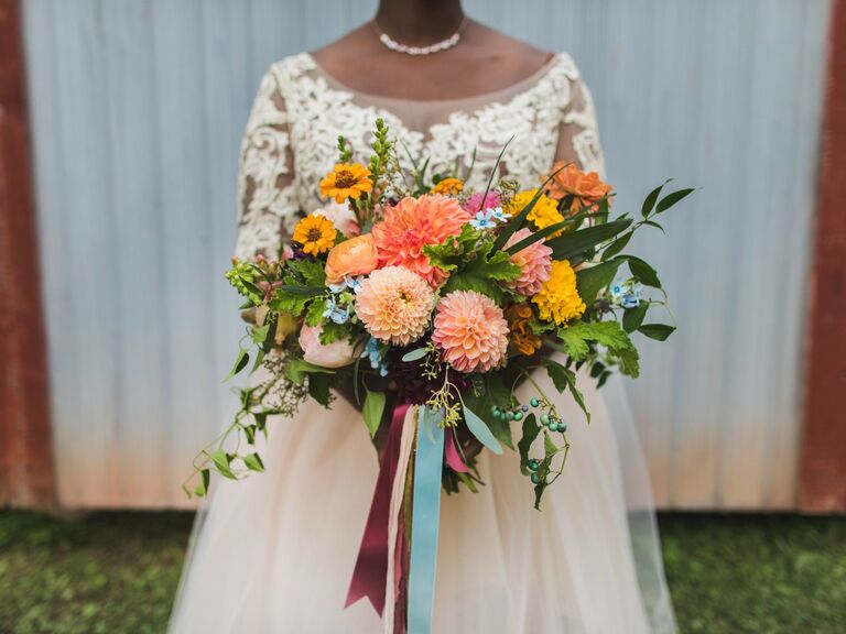 Bride holds a colorful and rustic bouquet of pink and orange dahlias. 