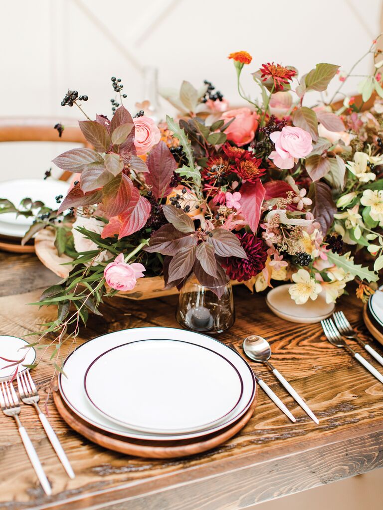 fall wedding centerpiece with burgundy leaves, pink flowers and greenery on bare wooden table