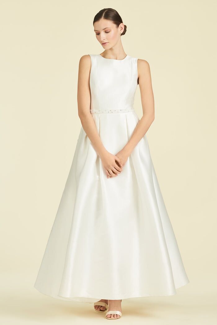 Model wears a chic white silk dress with a high neckline and a belted waist. 