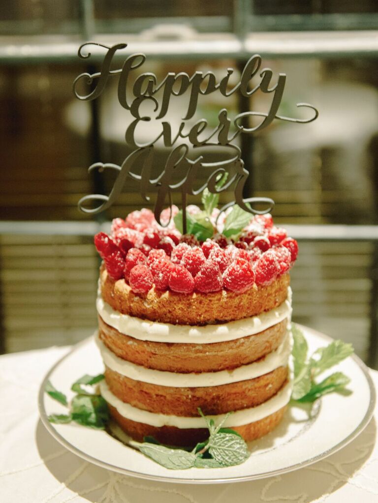 naked one tier wedding cake decorated with raspberries and happily ever after cake topper