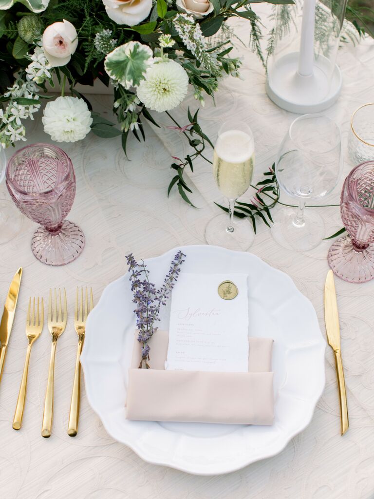 classic wedding place setting with pastel purple glassware, gold flatware, blush pink napkin and fresh lavender sprigs