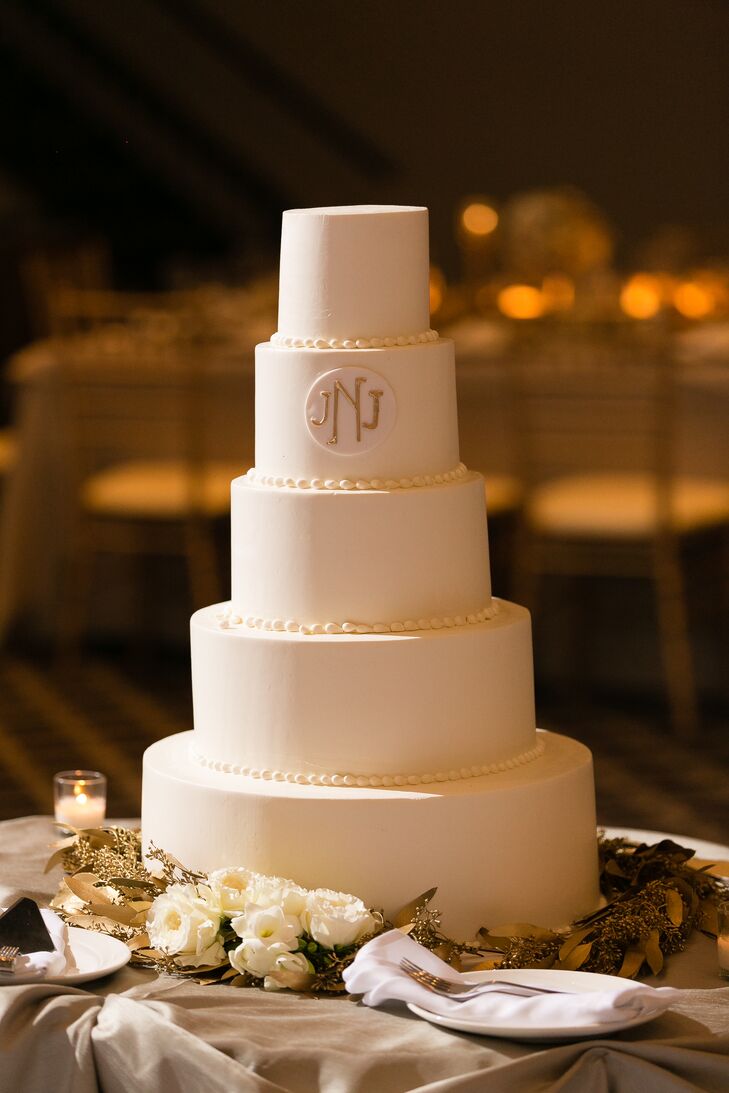 The wedding cake consisted of five tiers frosted in ivory buttercream with piping separating each tier and the couple’s minimalist gold monogram near the top. Surrounding the bottom of the cake were fresh white roses and gold foliage. “It was exactly as I dreamed it would be,” the bride says.