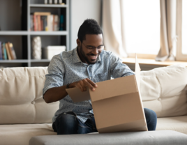 Man opening up care package on couch from partner
