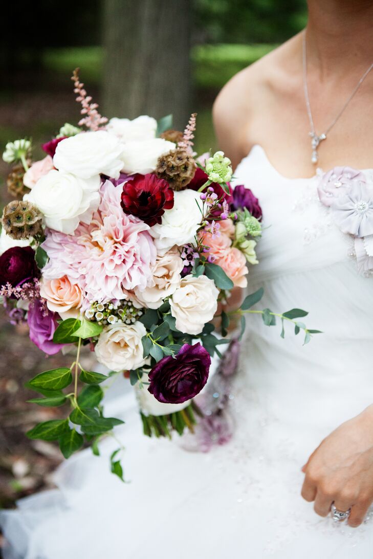 The bridal bouquet contained peach roses, lavender roses, purple wax flowers, light pink astilbes, scabiosa pods, light pink dahlias, and greenery, as well as white, burgundy and peach ranunculus.
