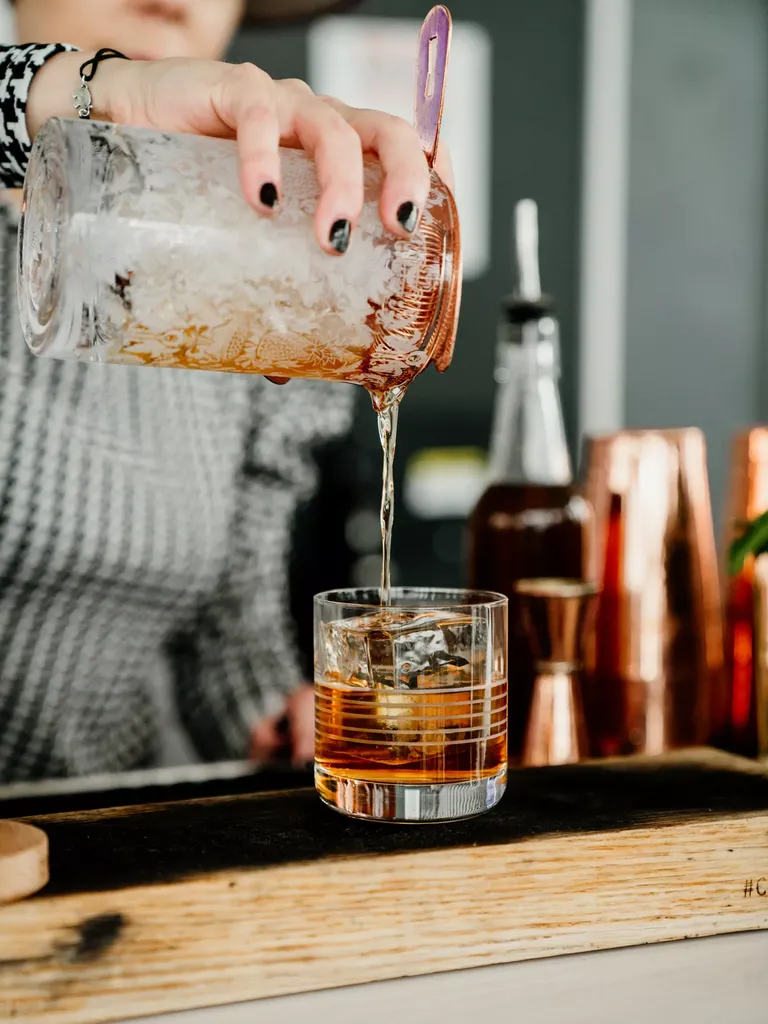 Bartender pouring whiskey sour drink into glass 