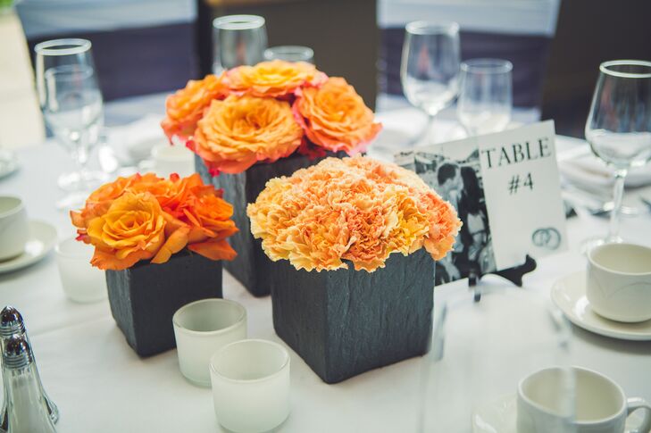 Orange roses and carnations were displayed in dark gray square boxes for the centerpiece decor.