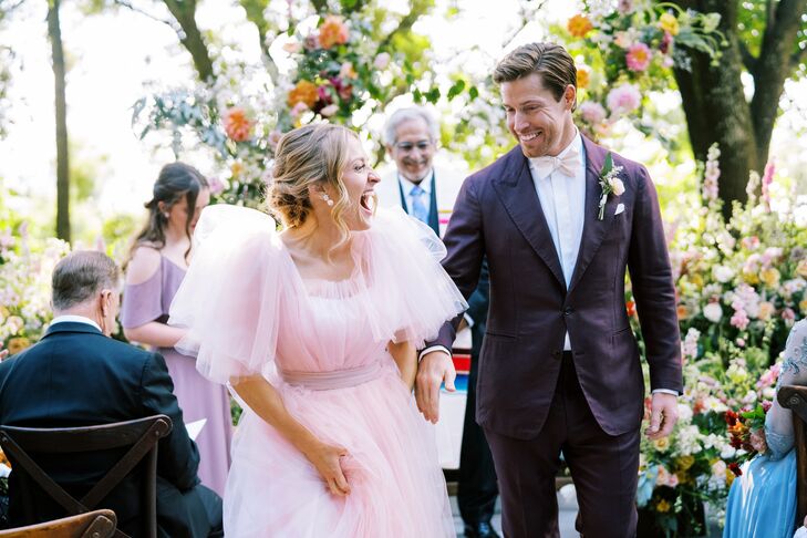 Bride in Blush Tulle Gown and Groom in Dark Maroon Suit Smiling During Recessional, Colorful