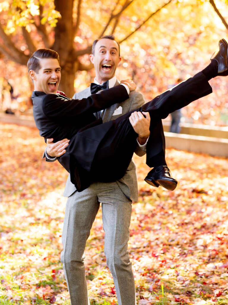 Two newly-engaged men smile in a fun pose among the autumn leaves